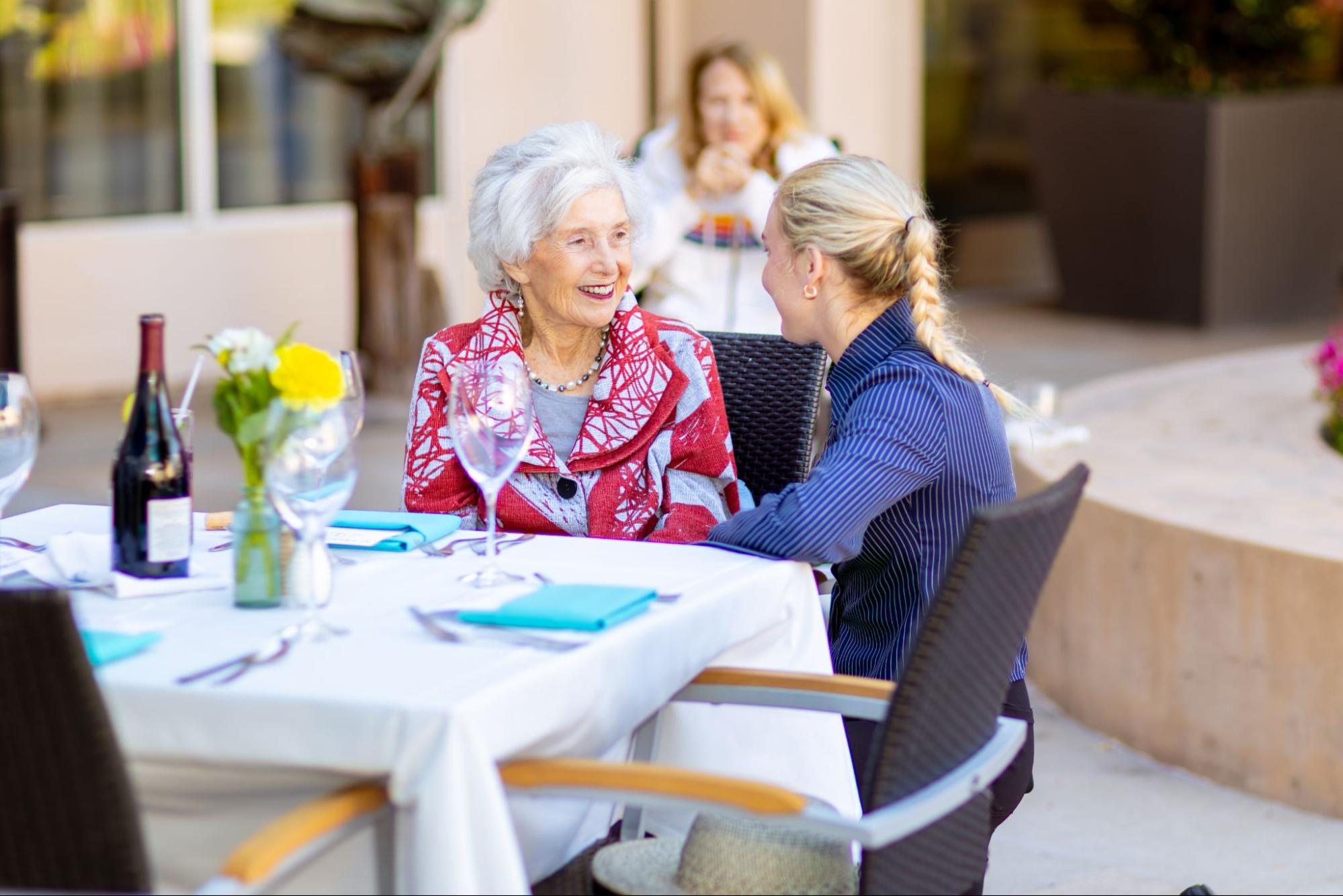 An elderly woman and a younger woman sitting at a table together, talking.