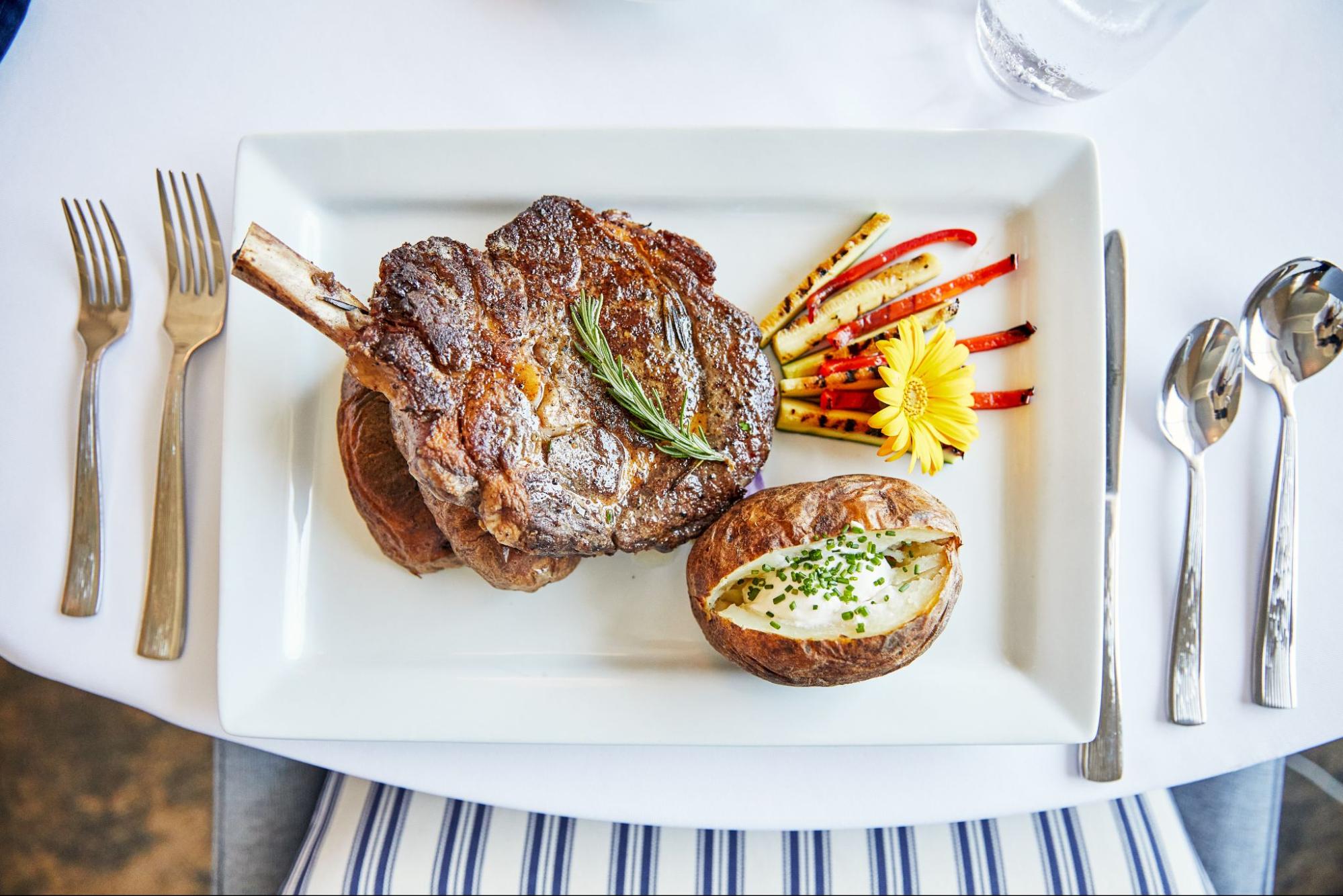 A high-end steak dinner, with a side of baked potato and vegetables.