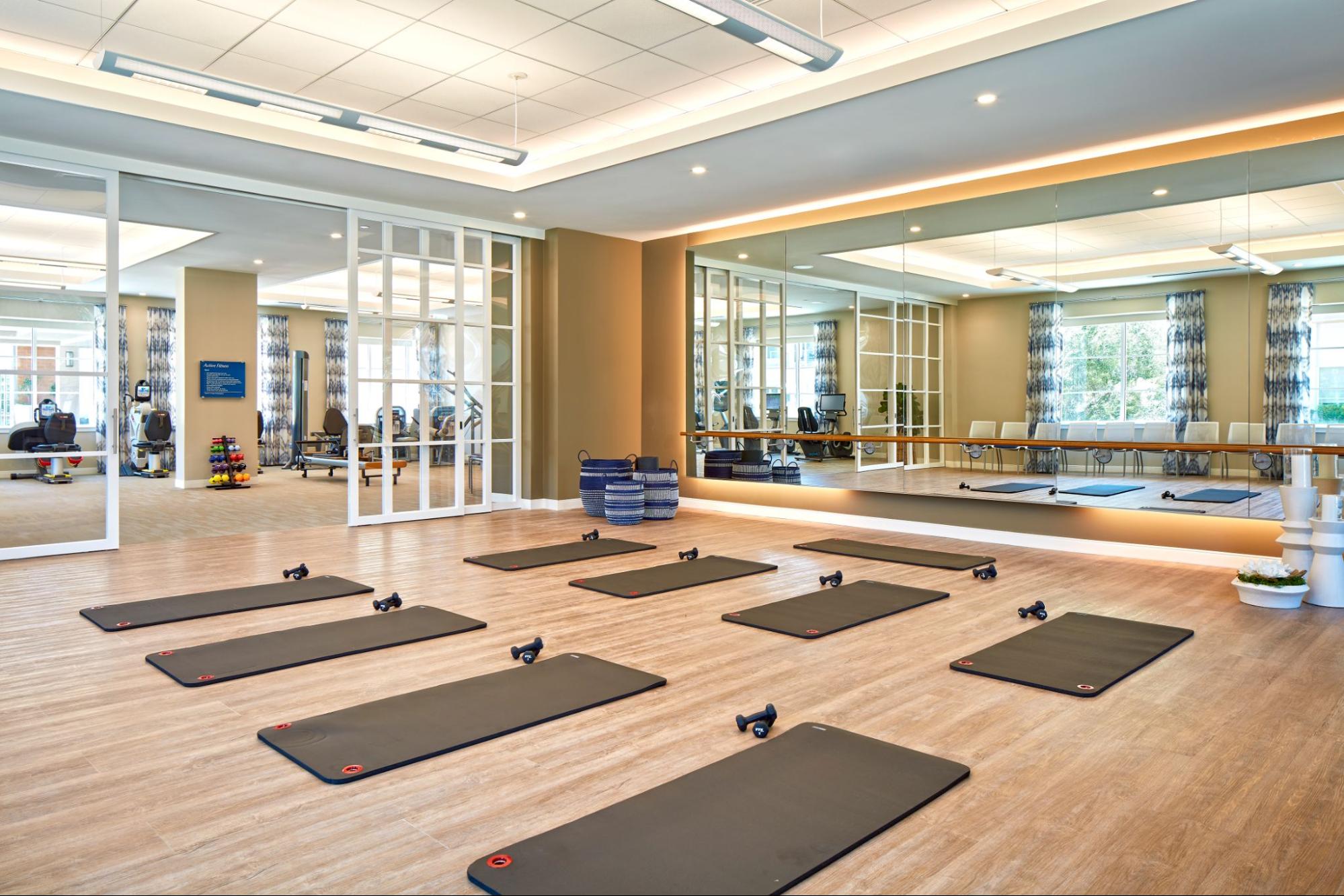 A fitness studio with a large mirror on one wall, and identical exercise mats with small dumbbells.