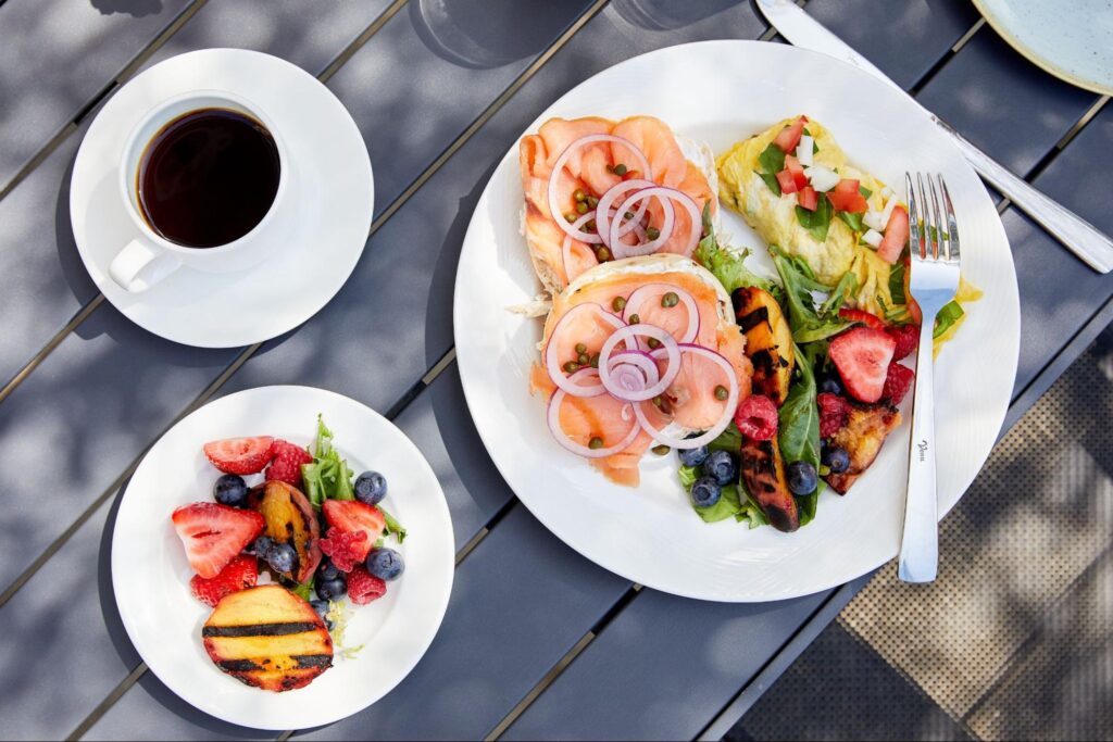 A beautifully plated breakfast, featuring eggs, smoked salmon, fruit, and a coffee.
