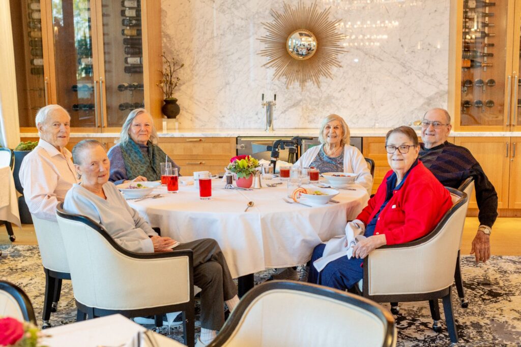 Six residents smiling and dining together at a round table in Vivante's upscale dining.